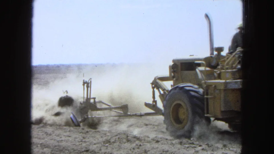 1965 Pueblo, Mexico frame with the tractor partly exiting right while dust and a trailing implement remain visible in the field.