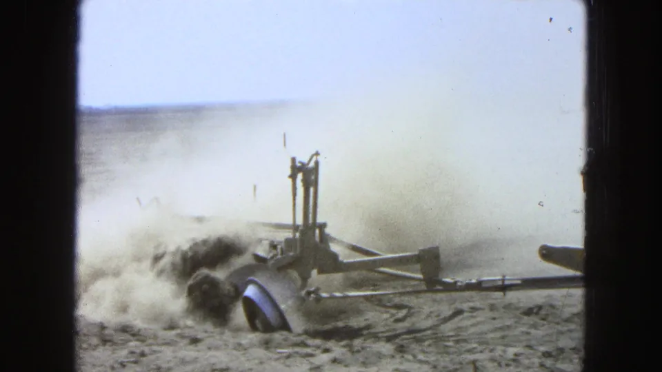 The tractor is mostly out of frame as its attached implement cuts through the dry Pueblo, Mexico field, throwing dust into the air.