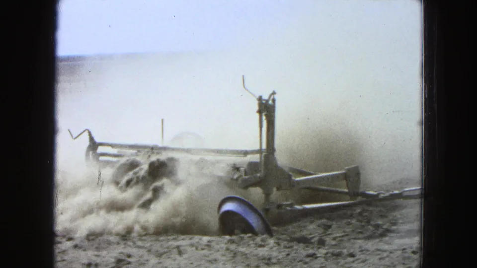 A closer 8mm view shows the plowing implement and wheel moving through dry soil in Pueblo, Mexico, with dust filling much of the frame.