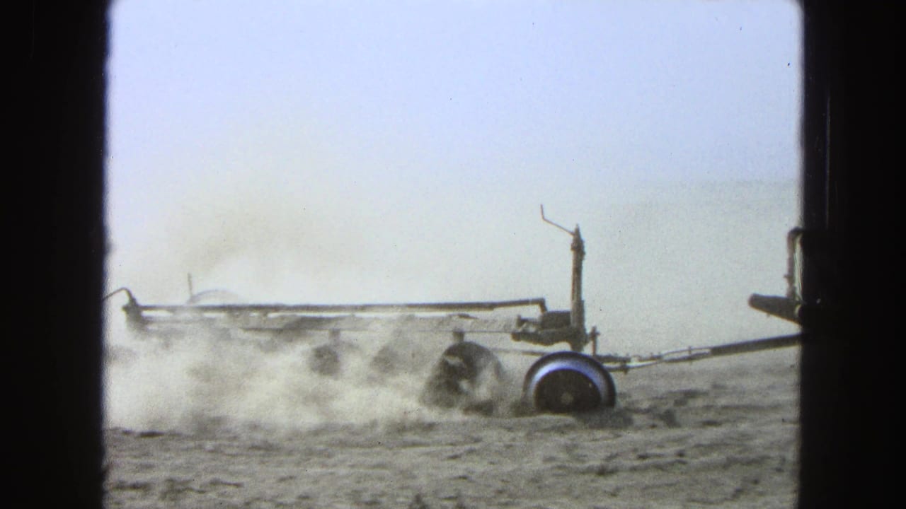 Tractor and plow moving across a dry field, throwing up dust behind dark film borders.