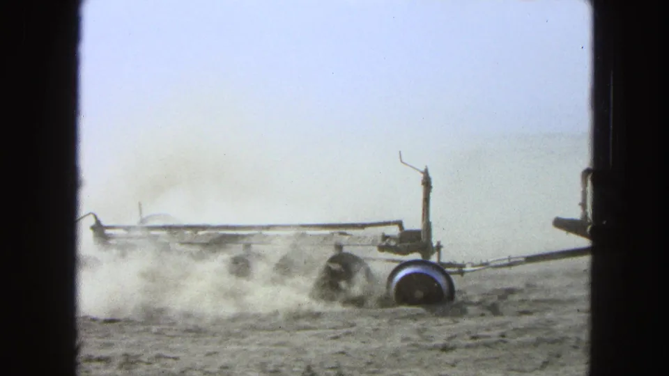 1965 Pueblo, Mexico home-movie frame of a tractor with plow equipment working a dry field as dust rises across the ground.