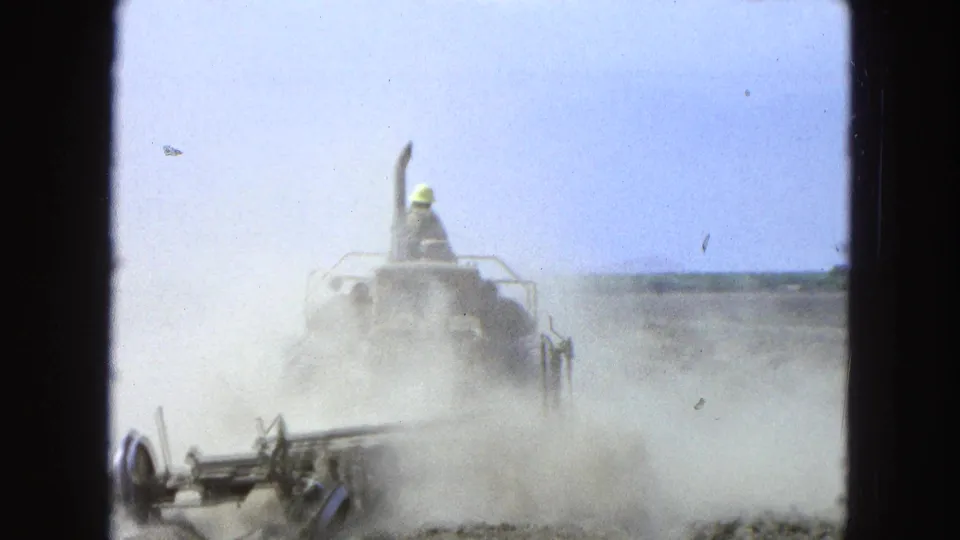 The tractor recedes through a heavy dust cloud in 1965 Pueblo, Mexico, with the plow attachment visible near the ground.