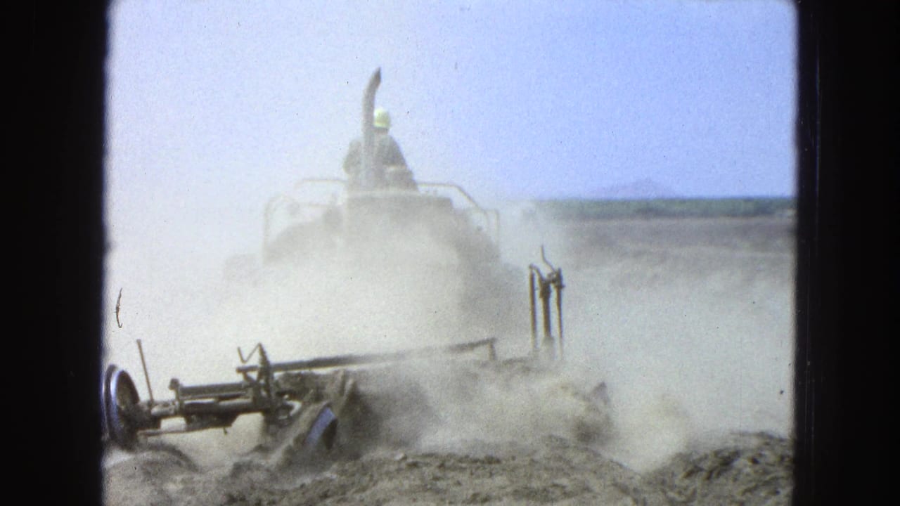 Tractor and plow moving through a dusty field with an operator visible above the machine.