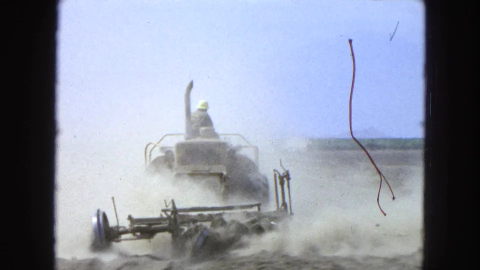 In 1965 Pueblo, Mexico, a tractor moves through a dusty field as the plow attachment turns dry soil.