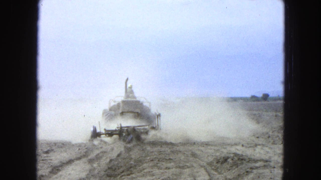 Tractor moving through sandy ruts while dust rises behind it.