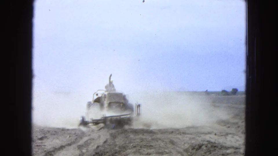 Distant tractor and driver in a dry Pueblo, Mexico field, partly obscured by pale dust under a bright sky.