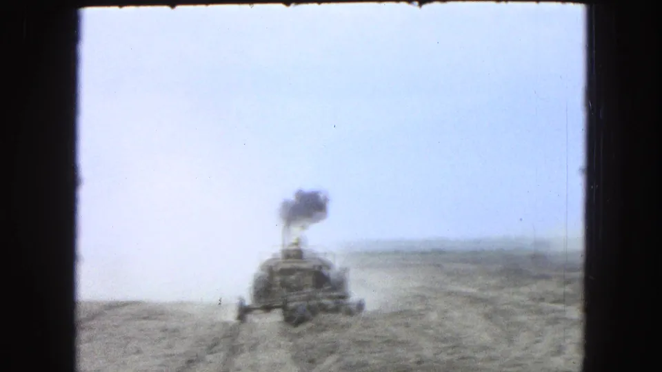 Rear view of the tractor in the arid field, with a dark plume rising above the machine and pale dust near the ground.