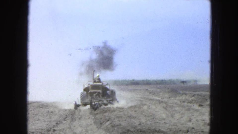 The tractor appears farther from the camera in the 1965 rural field, with dust near the wheels and a dark plume overhead.