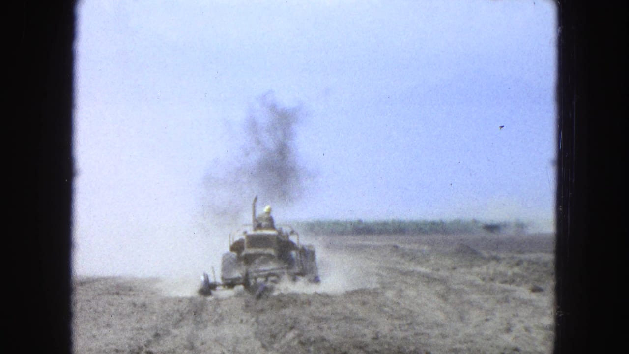 Tractor drives across a dusty field with a driver visible at the controls.