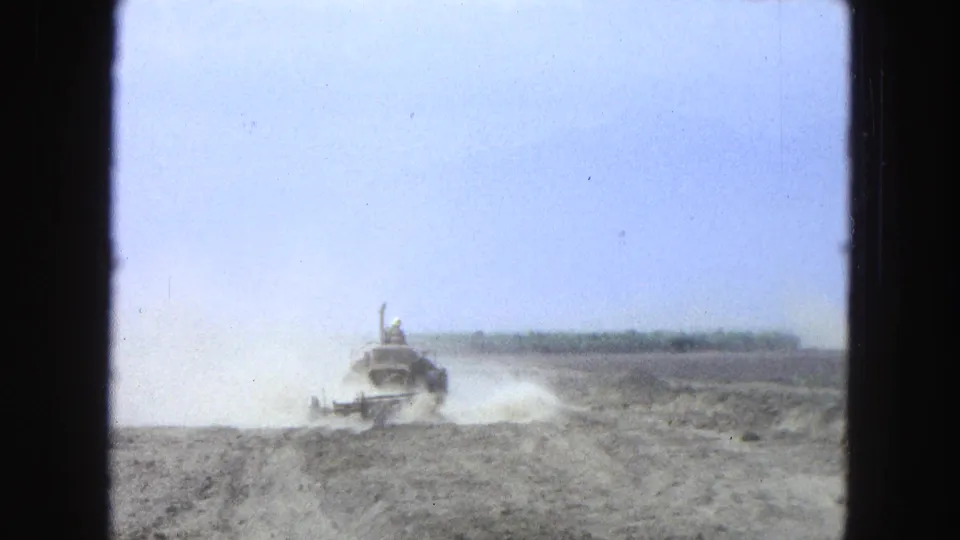 The tractor continues across the dry rural field in 1965 Pueblo, Mexico footage, with the driver small and dust spreading low over the soil.