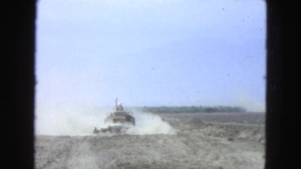 A tractor and visible driver work through uneven dry soil in 1965 Pueblo, Mexico home-movie footage, with dust blown across the field.