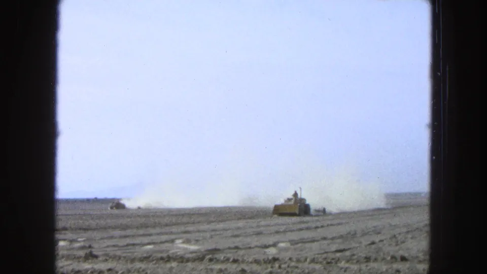 A yellow tractor crosses a dry Pueblo, Mexico field in 1965 home-movie footage as another machine raises dust in the distance.