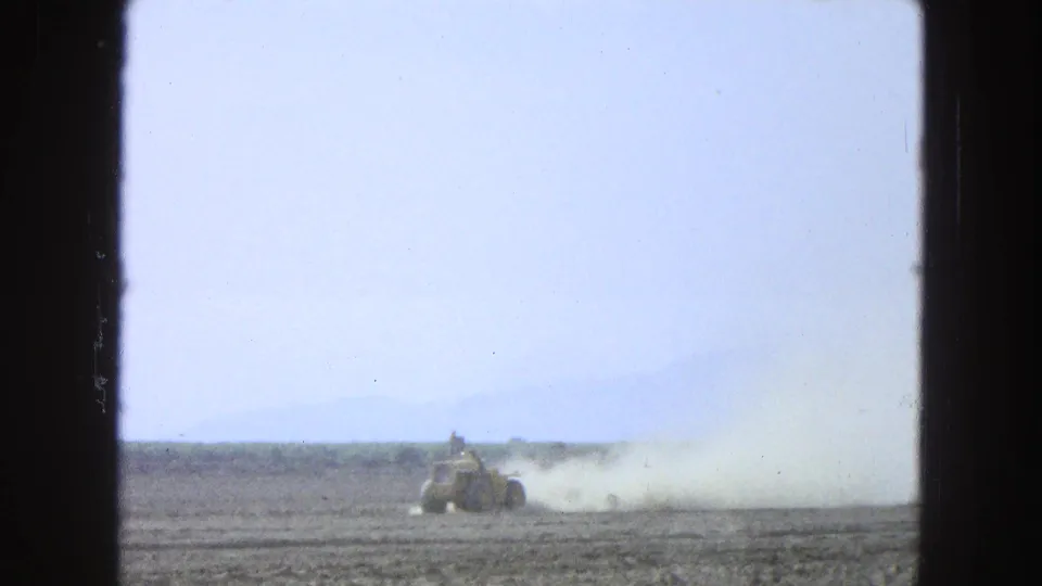A yellow tractor moves through a dusty Pueblo, Mexico field in 1965 8mm footage, with the operator only indistinctly visible.