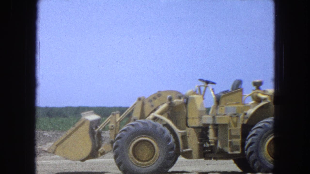 Yellow front-end loader and tractor crossing a dry field under a blue sky.