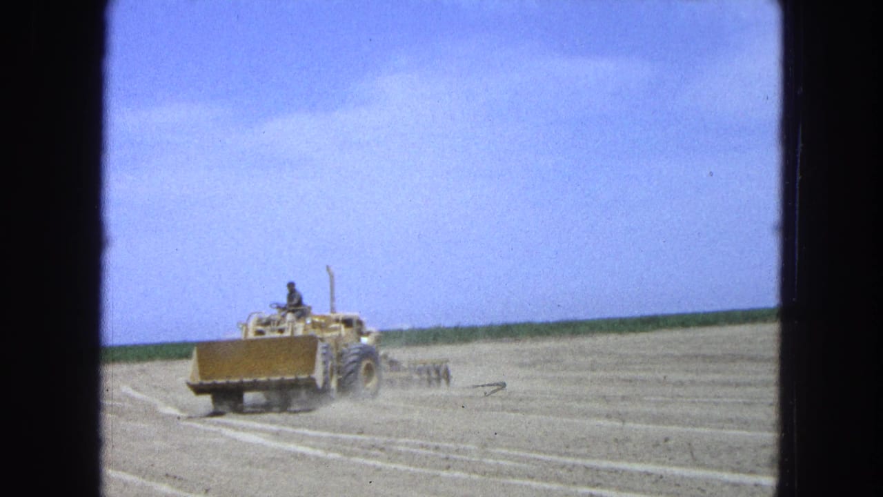 Yellow dozer crosses a dry field under a blue sky.