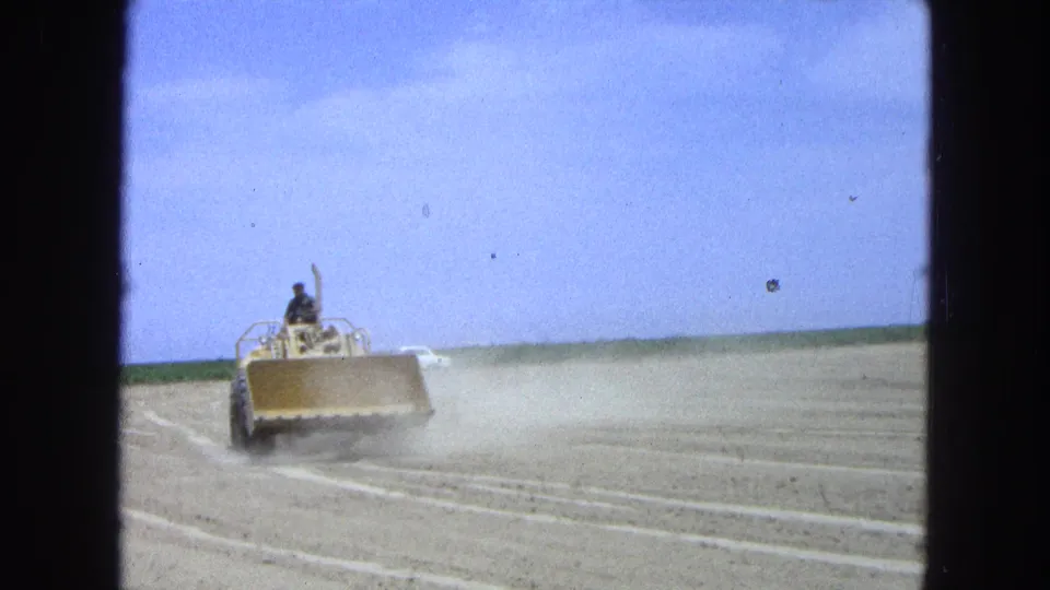 A yellow dozer advances through the arid field, raising dust as it works the soil in 1965 Pueblo, Mexico footage.