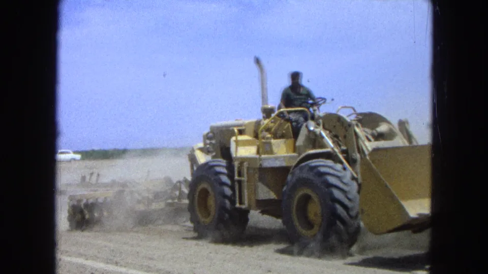 A closer 1965 Pueblo, Mexico view shows the dozer operator seated above large tires as equipment disturbs the dry soil.