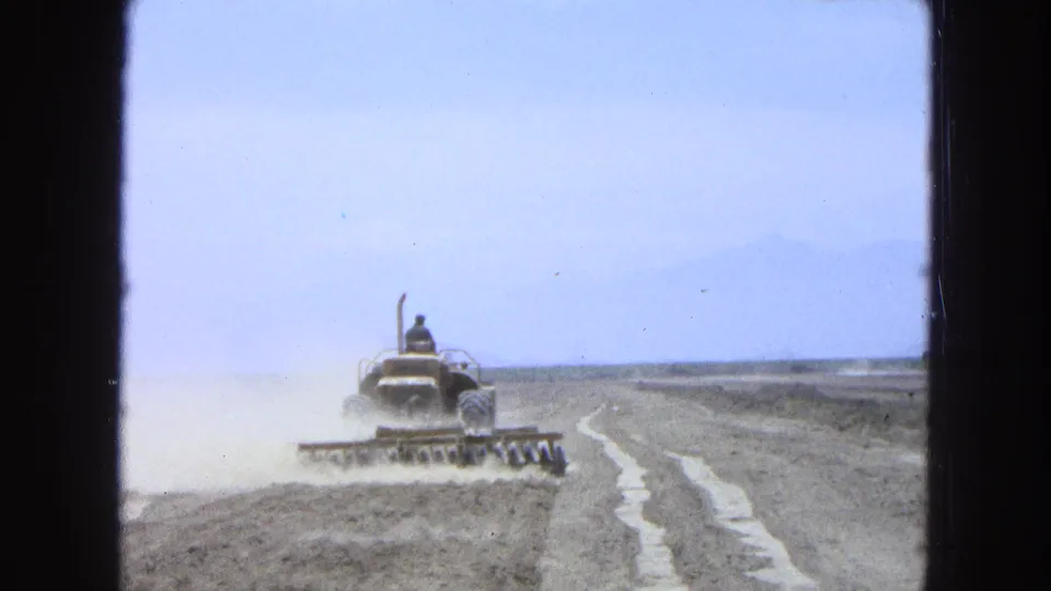 Rear view of a tractor and disc harrow in a dry rural field, filmed on 8mm in Pueblo, Mexico in 1965.