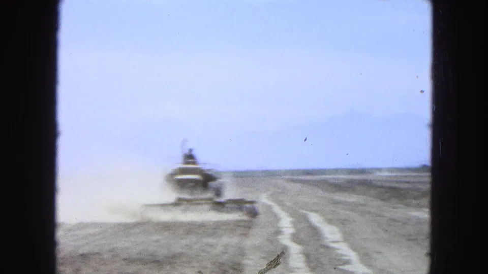 Soft, distant 8mm frame of the tractor receding through dust across an open Pueblo, Mexico field in 1965.