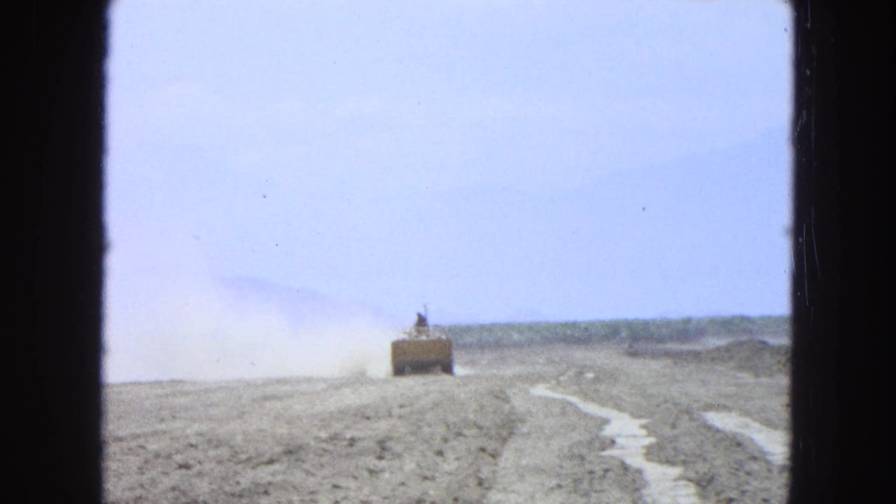 Distant tractor crossing a dry field with dust rising behind it.