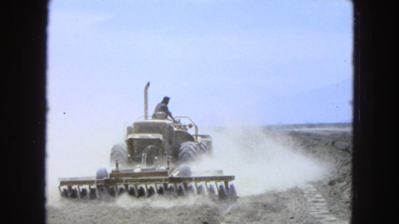 The tractor continues across a dry Pueblo, Mexico field in 1965, pulling a disc harrow as dust trails behind it.