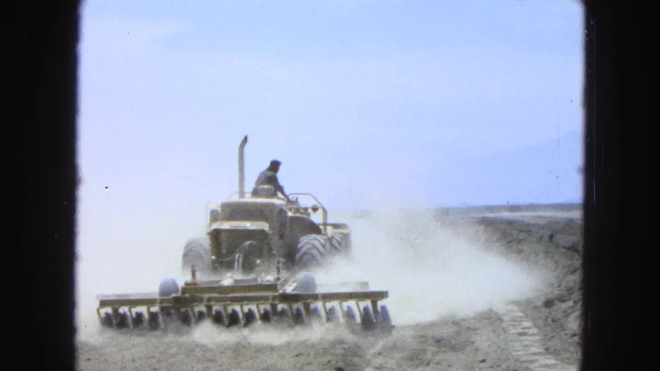 The tractor continues across a dry Pueblo, Mexico field in 1965, pulling a disc harrow as dust trails behind it.