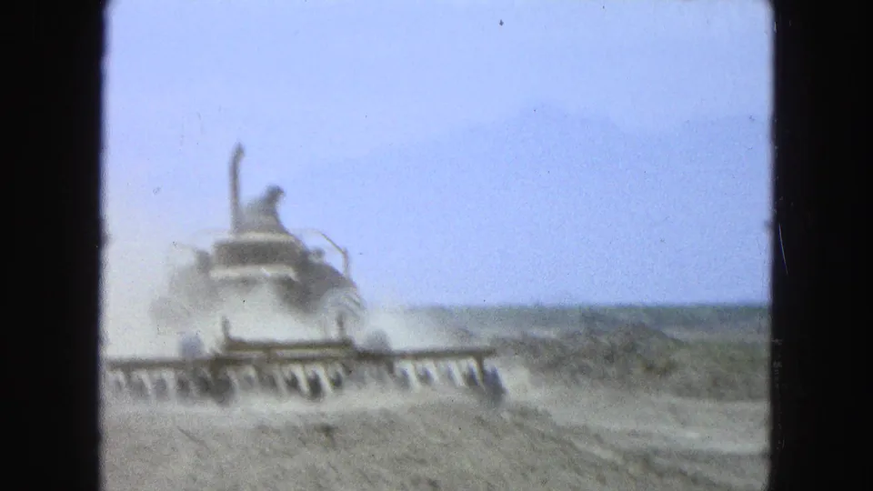 The tractor appears partly softened by motion and dust as it pulls the harrow across the dry Pueblo, Mexico field.