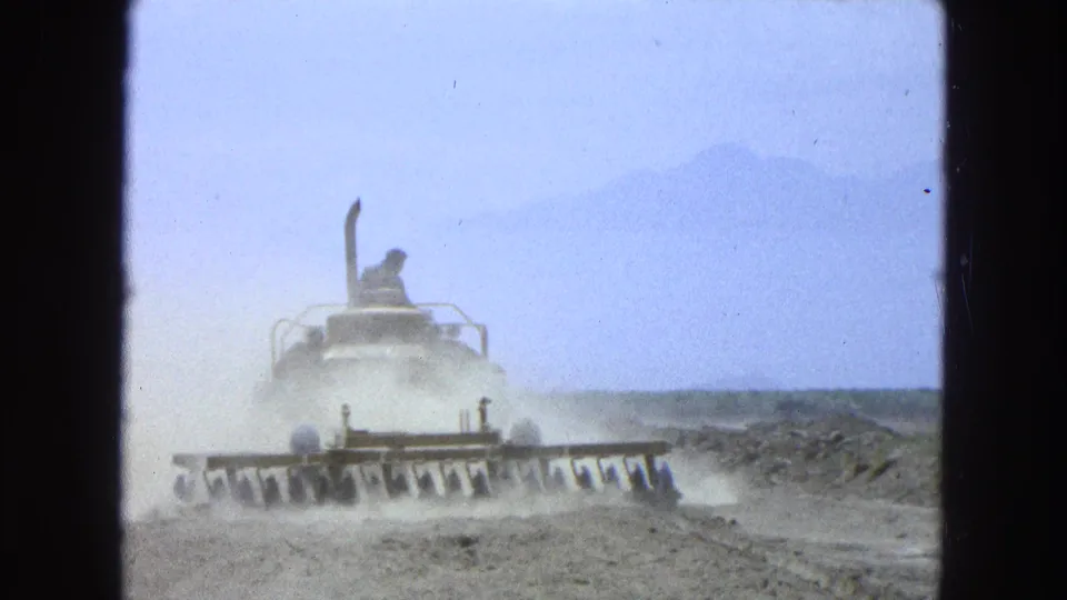 1965 Pueblo Mexico footage shows a tractor with broad blades working dry soil while dust rises behind it.