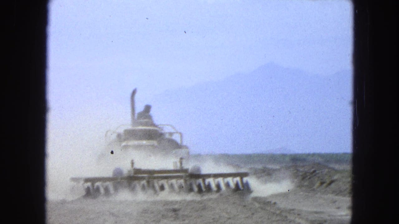 Tractor advances through dust on rough land with mountains faintly visible.
