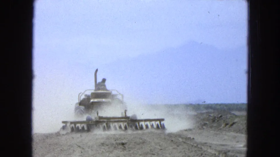 Soft 8mm view of a tractor operator working dry open ground in Pueblo, Mexico, with mountains faintly visible.