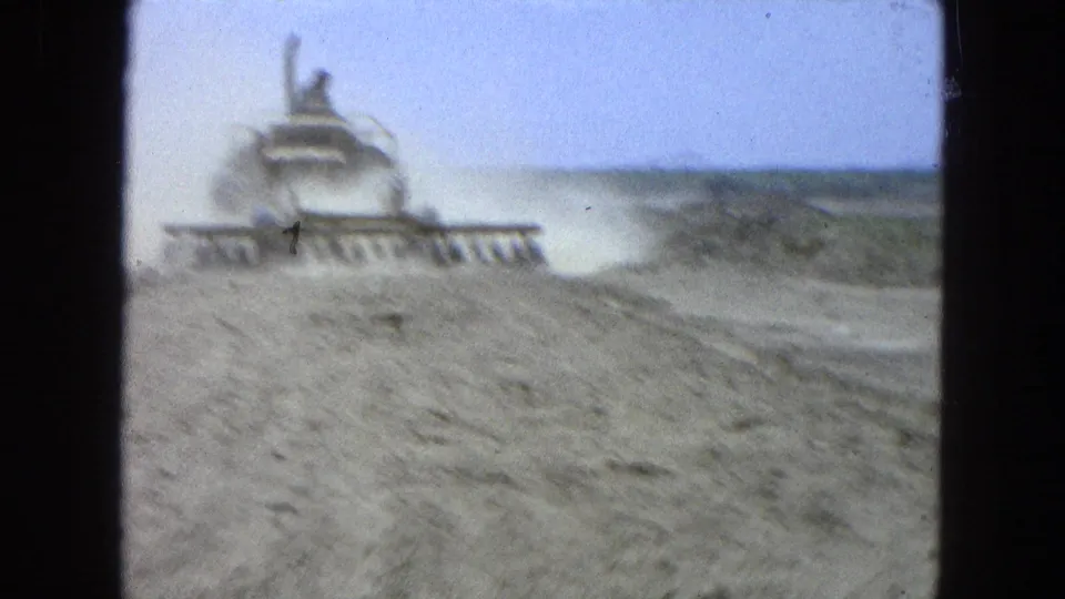 1965 home-movie frame showing a tractor receding across a dusty rural field in Pueblo, Mexico.