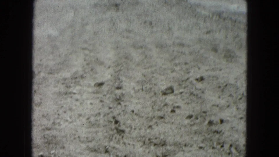 1965 8mm home-movie frame from Pueblo, Mexico showing pale rocky ground in an arid landscape.