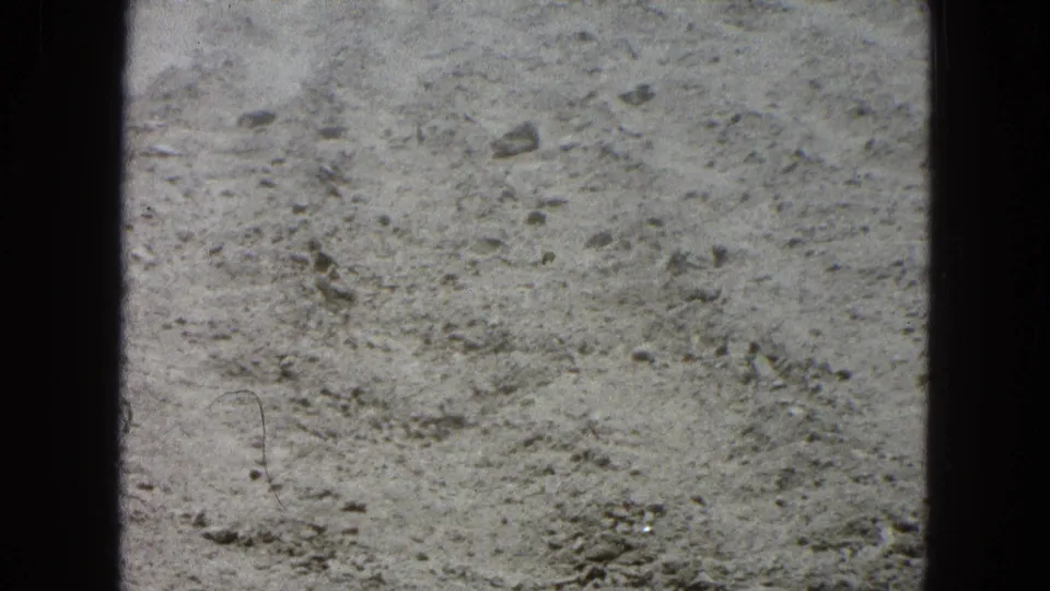 Close, handheld 8mm view of dry rocky soil from the supplied 1965 Pueblo, Mexico footage.