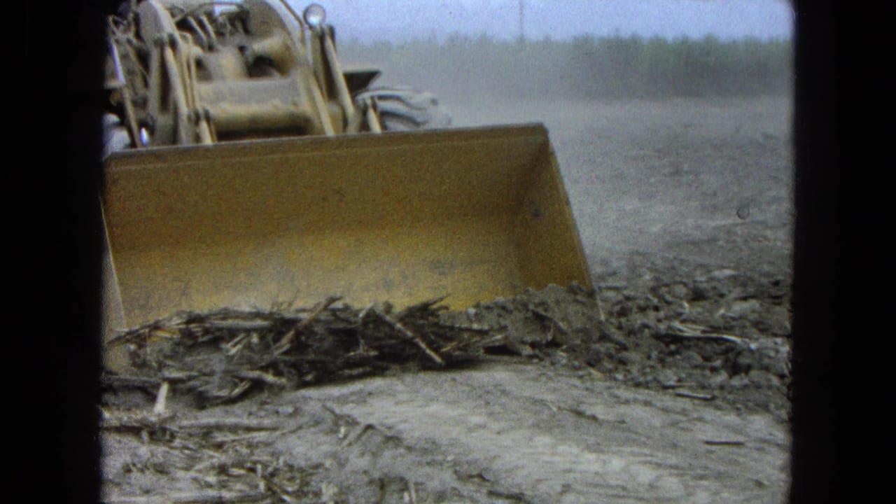 Yellow tractor blade pushing dirt and crop residue across a field.