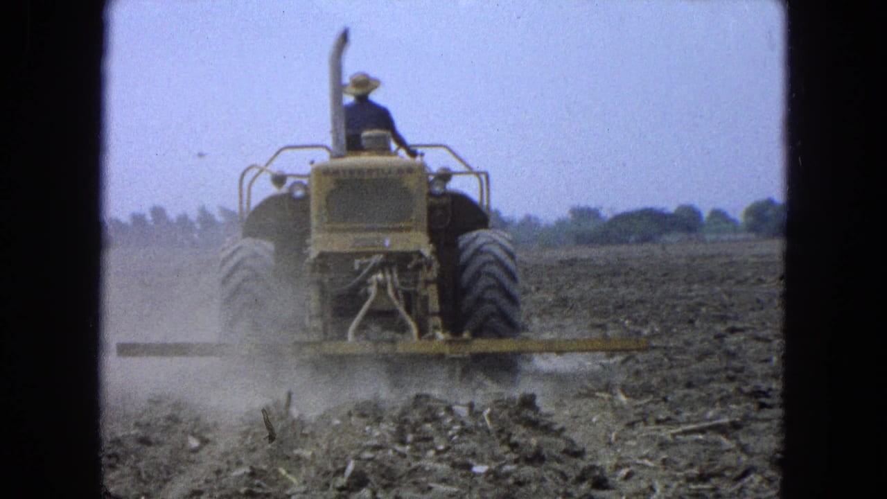 The tractor continues forward through the field, with the tilling attachment disturbing dry soil and raising dust in rural Mexico footage.