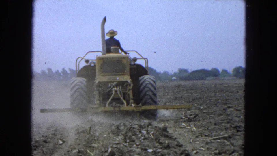 Final frame of the clip shows the farmer and tractor still moving across the dry field, with dust rising from the attached tiller.