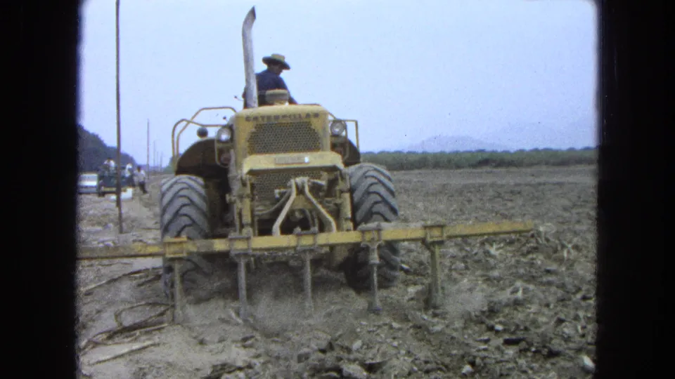 1965 Pueblo Mexico frame showing the tractor from behind as the tillage attachment disturbs dusty soil.