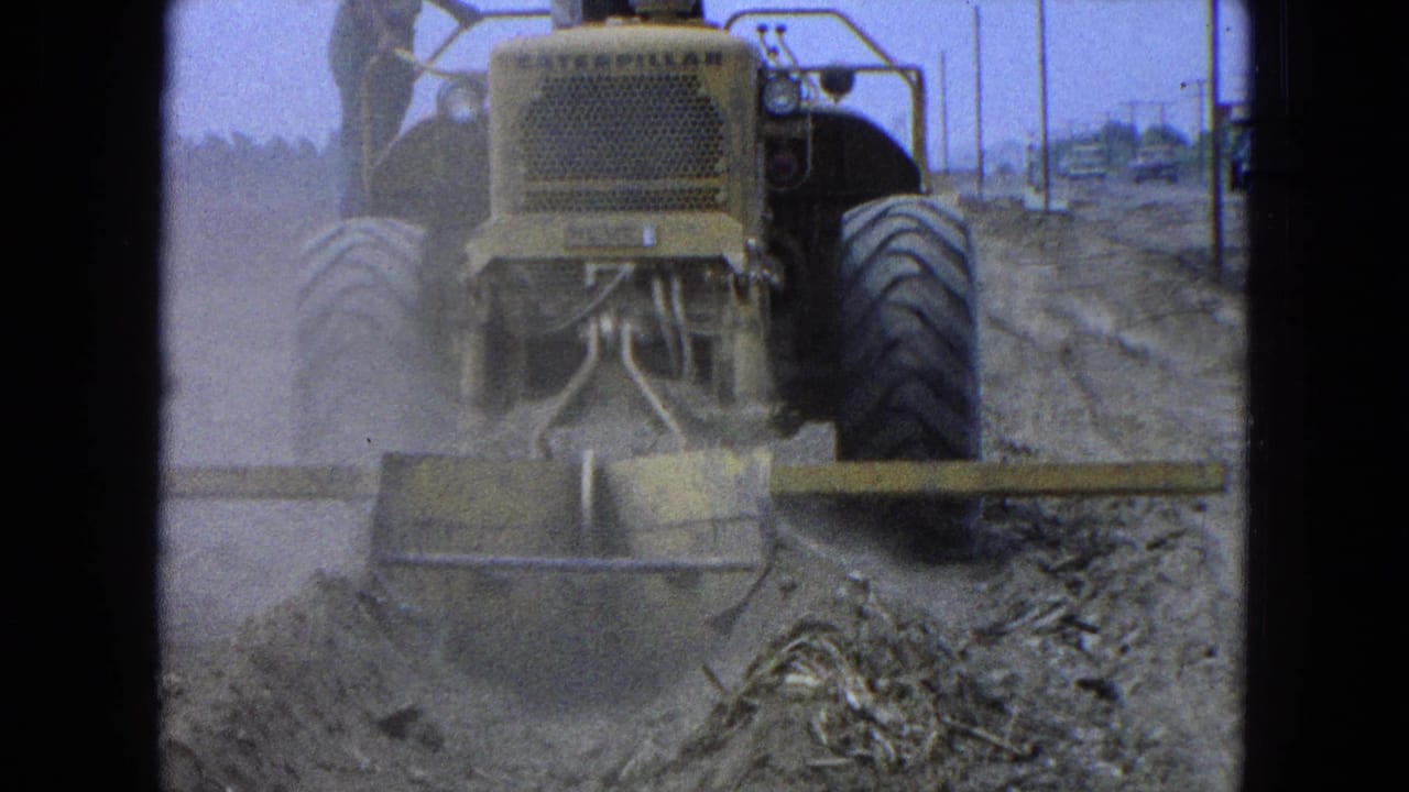 Rear view of the Caterpillar bulldozer grading earth in Pueblo, Mexico, with utility poles and distant structures in the background.
