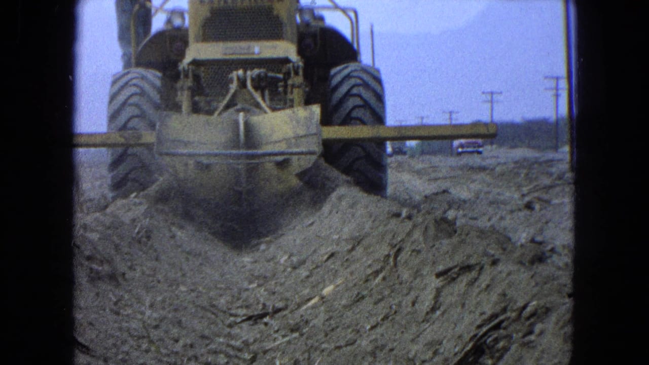 Rear view of a yellow earthmover pushing dirt on a dusty construction site.