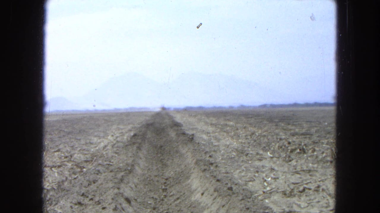 Wide dry field with a long trench leading toward a distant earthmoving machine.
