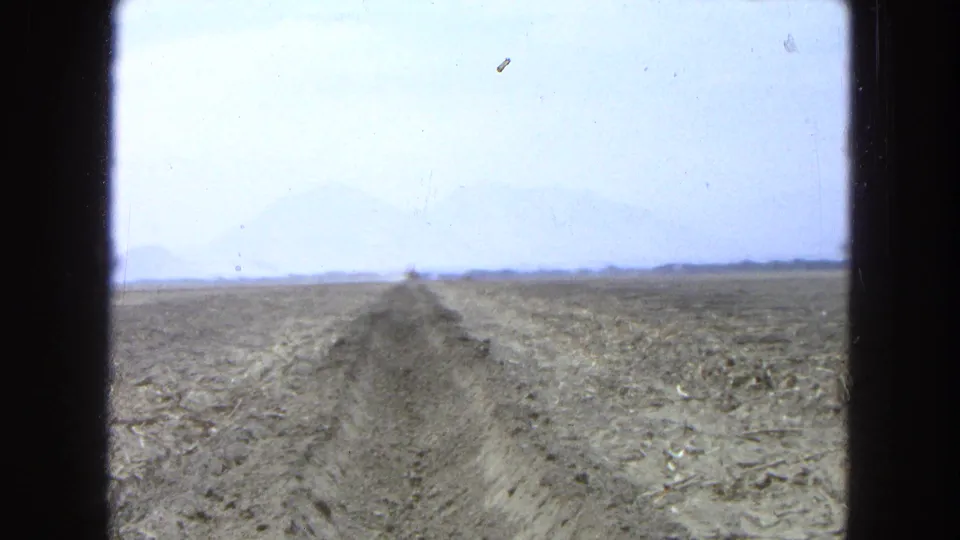 1965 Pueblo, Mexico 8mm frame showing a trench through an arid field, distant machinery, hazy mountains, and visible film borders.