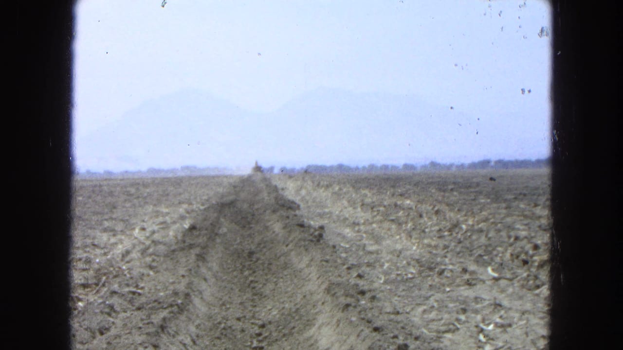 Dry field and trench with earthmoving equipment far ahead near the horizon.