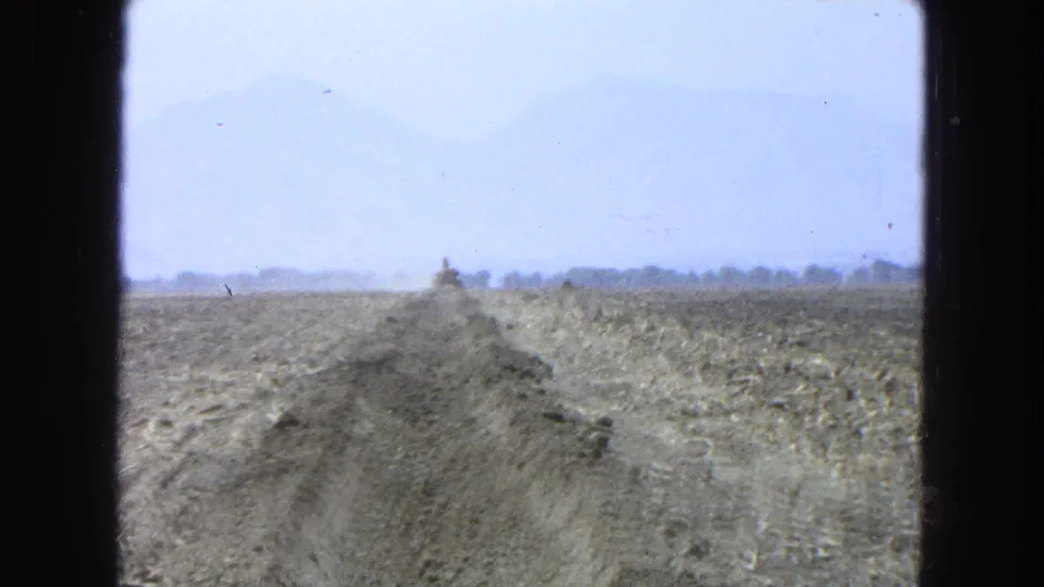 1965 Pueblo, Mexico 8mm frame showing the trench line from a low vantage point, with a small earthmoving machine ahead and hazy mountains behind.