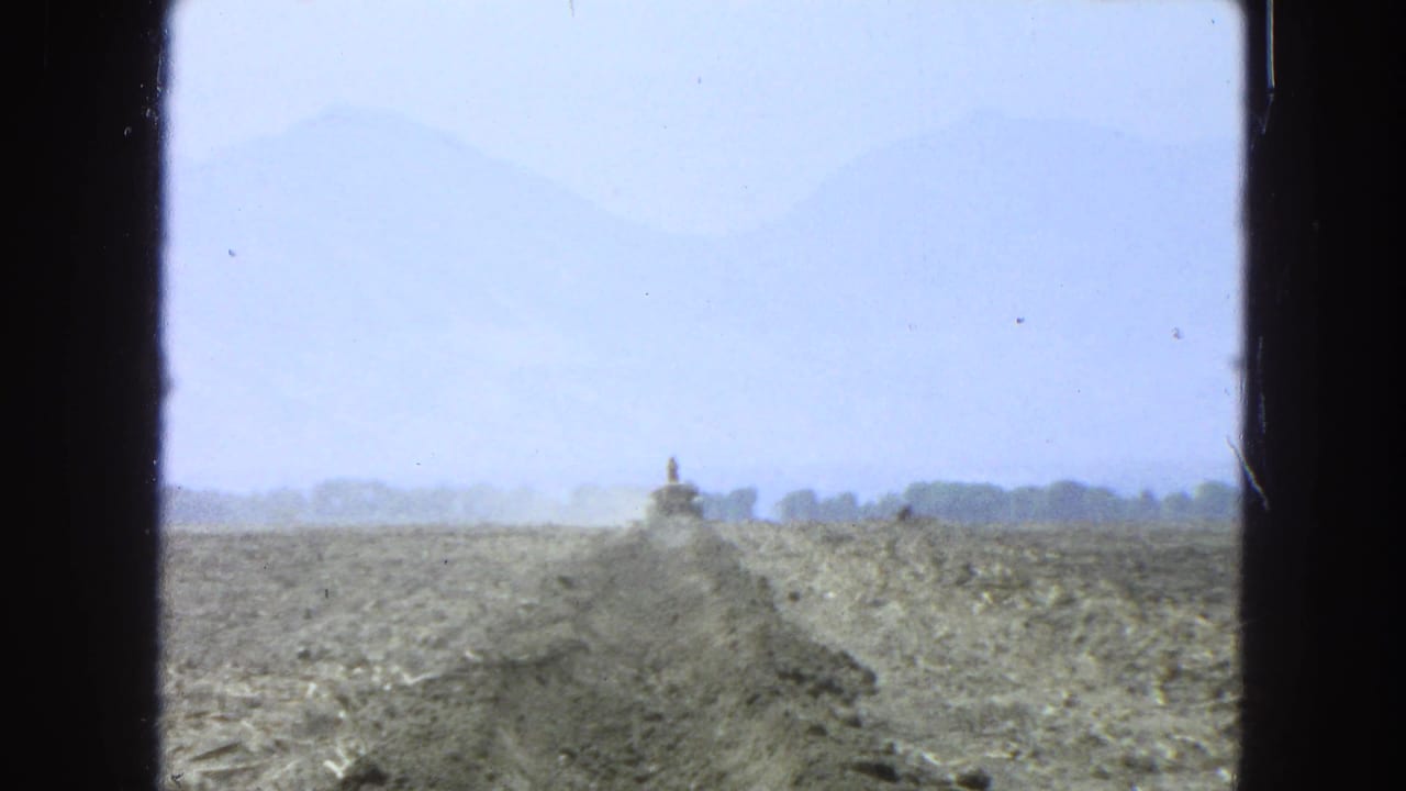 Dirt road or trench stretching across arid land toward distant mountains, framed by dark window edges.