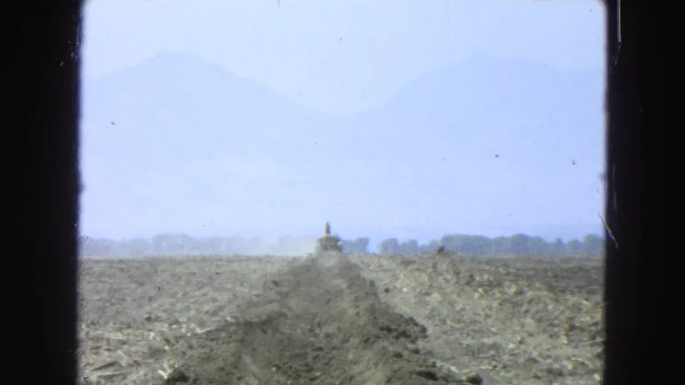 1965 Pueblo, Mexico home-movie frame showing a dusty road or trench in an open rural landscape, seen through dark window framing.