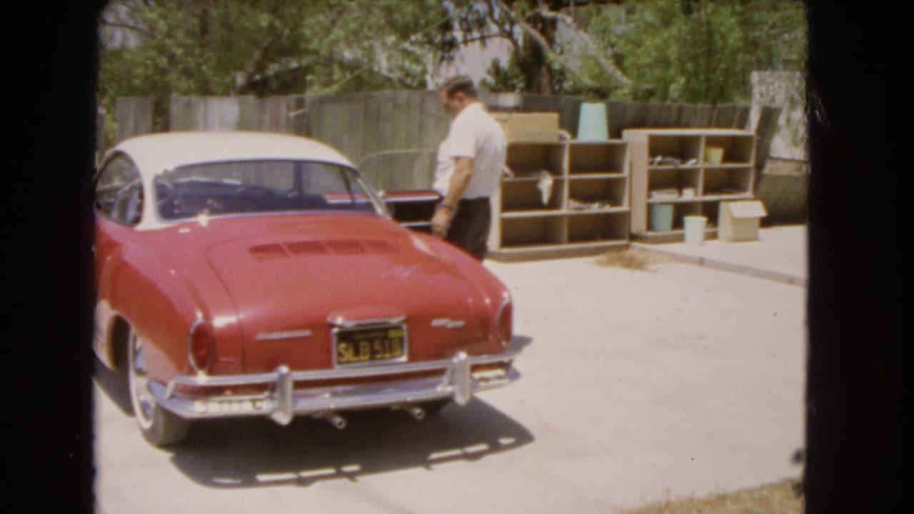 Man in a white shirt stands beside the driver's side of the red and white coupe.