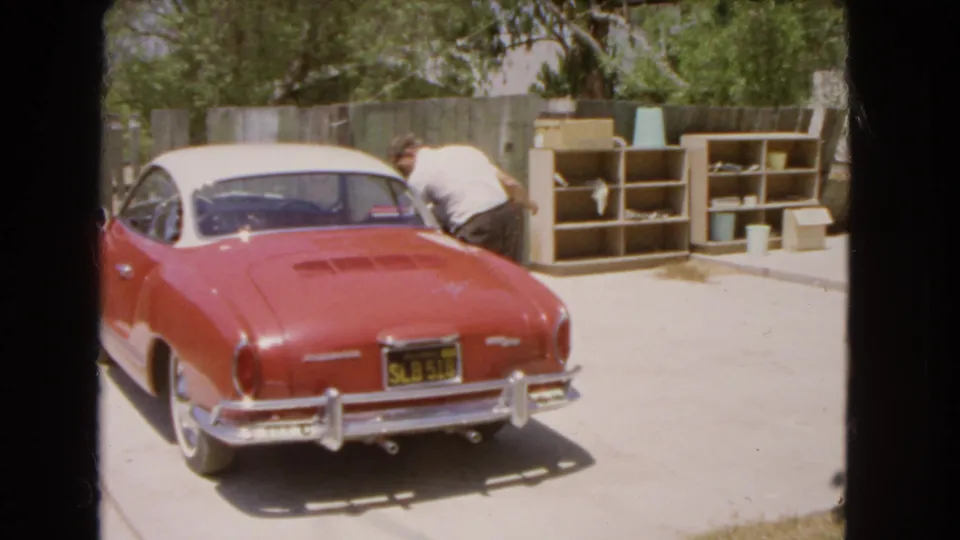 The man leans over the driver's side of the red and white Volkswagen Karmann Ghia during the 1966 Barstow home-movie shot.