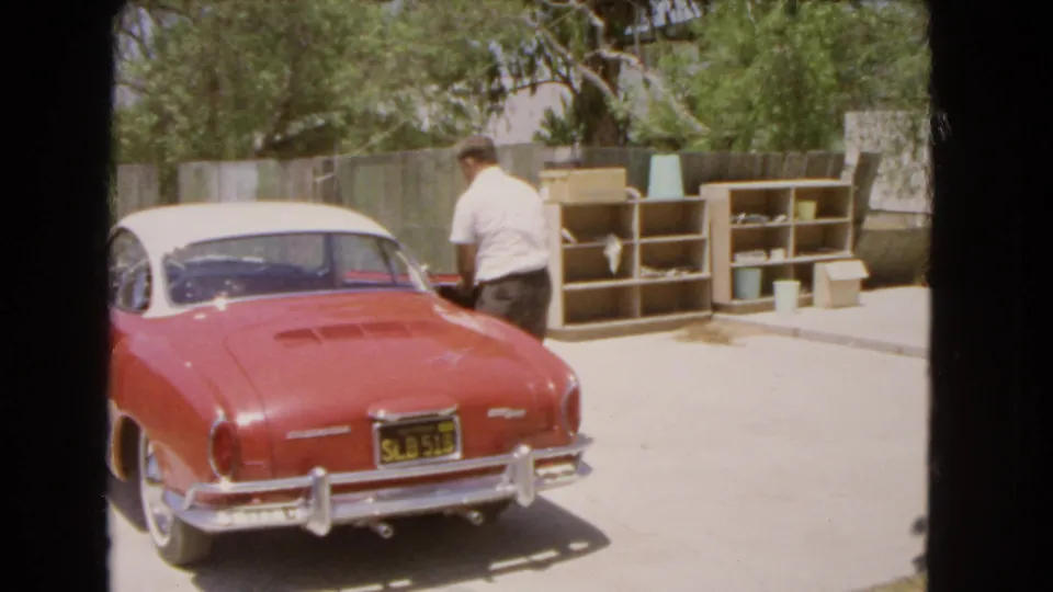 A 1966 Barstow frame shows the man beside the driver's side of the red and white Volkswagen Karmann Ghia in a bright backyard driveway.