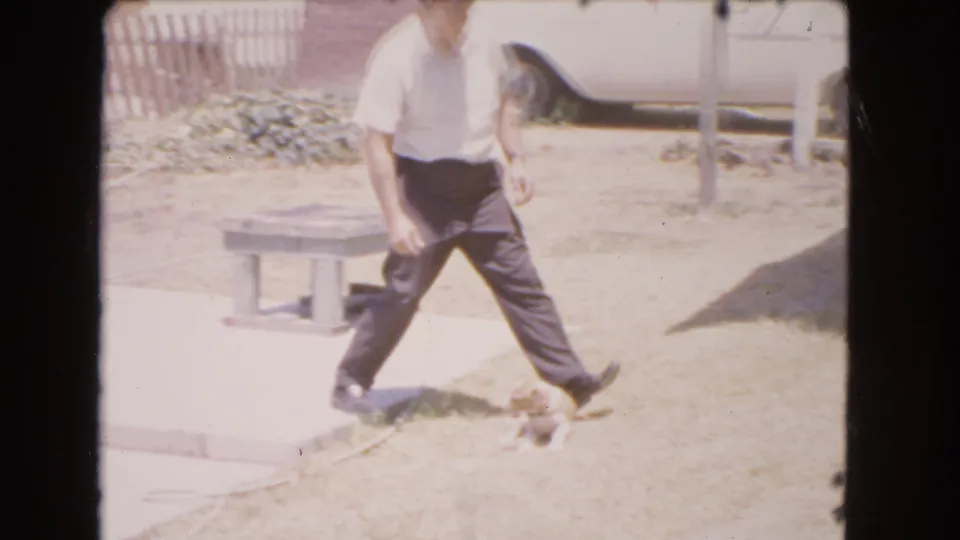 1966 Barstow home-movie frame showing the man stepping through the yard as the small dog moves beside him.