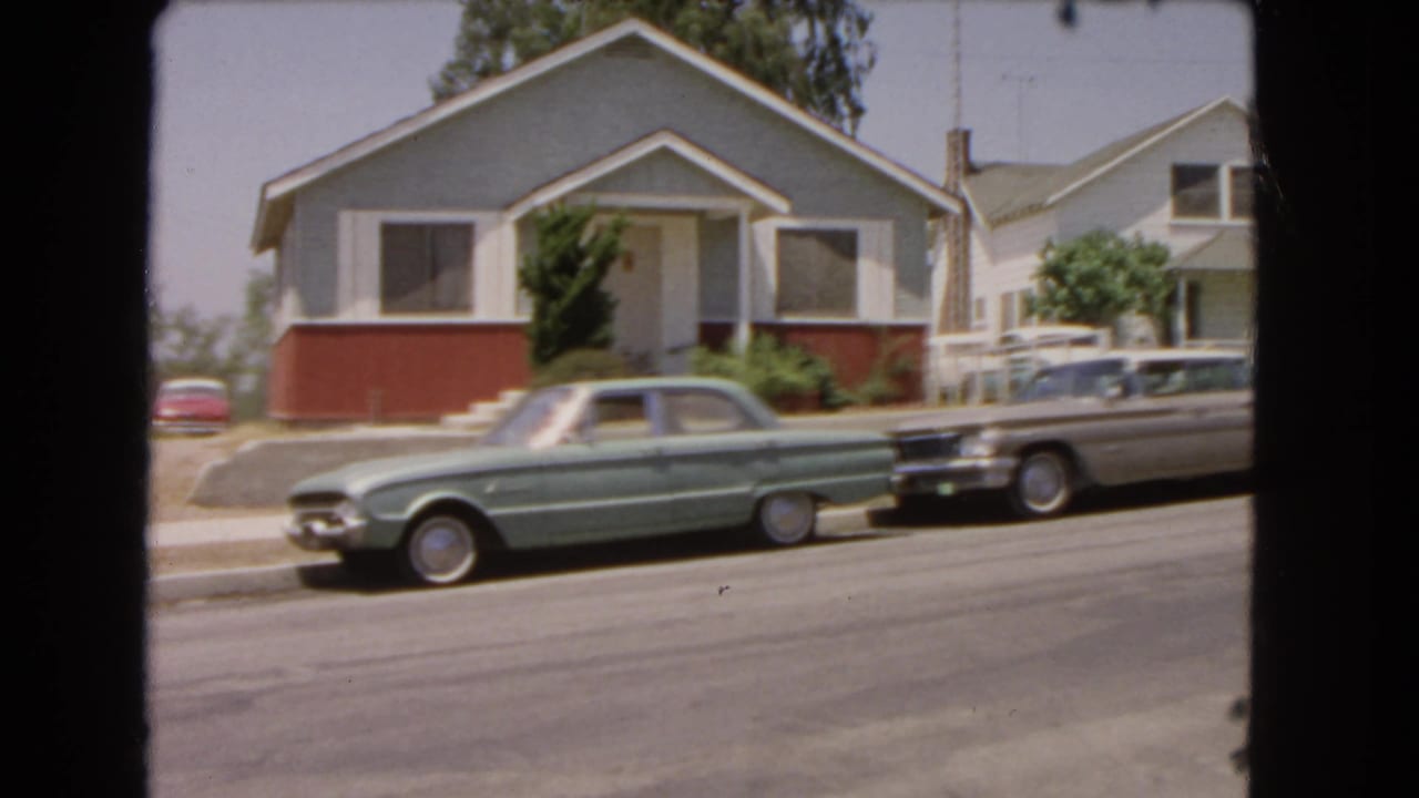 1966 Barstow frame with a green sedan and silver station wagon parked before a small residential house in daylight.